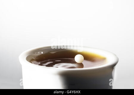 Tropfen Milch balancing und reflektiert an der Spitze, so wie es eine Tasse schwarzen Kaffee trifft Stockfoto