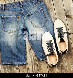 Satz von Reisen Elementen einschließlich Jeans und Sneakers.  Verschiedene Objekte und Passagiergepäck auf grauem Hintergrund aus Holz. Nach oben Stockfoto