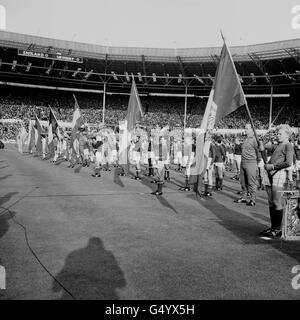 Parade der Flaggen der konkurrierenden Nationen auf dem Feld im Wembley-Stadion in London, während der die Königin ihr das England-Team und ihre Gegner Uruguay vorgestellt wird, nachdem sie das erste WM-Spiel des Turniers eröffnet hatte. * hinter der Königin sind die Beamten und Spieler abgebildet. Stockfoto