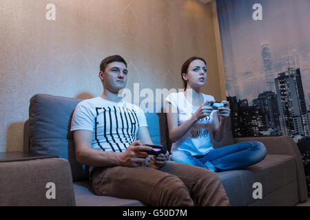 Seitenansicht der ein junger Mann und eine Frau so leidenschaftlich über den Prozess der ein Spiel und sitzt auf einer Couch zu Hause spielen Video-Spiele zusammen. Stockfoto