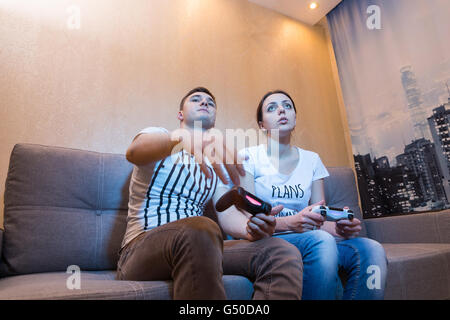 Junges Paar warten auf Ergebnisse der Video-Spiel, während sie auf einer Couch zusammen vor dem Fernseher zu Hause in einer entspannten Sitzen Stockfoto