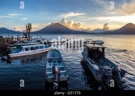 Sonnenuntergang über die Vulkane der Lago de Atitlán in Guatemala und Wasser taxis Sit festgemacht an den Docks des Ferienortes Panajachel Stockfoto