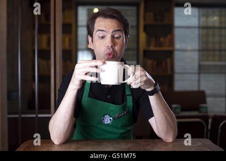 Jimmy Carr legt eine grüne Schürze an, um Amelia Hemphill aus London bei Starbucks in der Conduit Street, London, zu bedienen, um ihren neuen stärkeren britischen Latte zu lancieren. Stockfoto