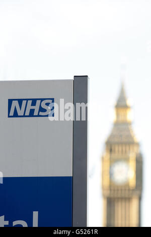 Ein NHS-Schild am St. Thomas' Hospital, mit Big Ben im Hintergrund, in Westminster, im Zentrum von London Stockfoto