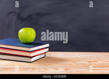 Zurück zum Schulkonzept mit grünem Apfel und Bücher auf Schreibtisch vor gelöschten schwarzen Tafel. Stockfoto