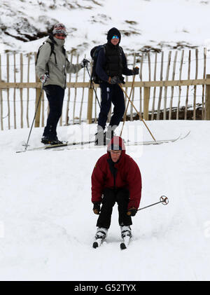 Die Skifahrer Sam und Paul Cunningham aus Perth beobachten Terry Cunningham beim Skifahren im Skigebiet Glenshee in den Cairngorms. Stockfoto