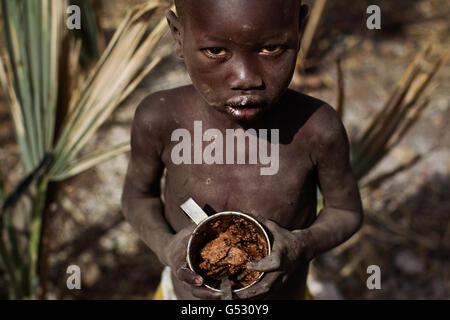 Ein kleiner Junge mit einer Tasse harten Keks zum Essen im Doro Flüchtlingslager in Bunj, Maban, im Bundesstaat Upper Nile Blue Nile im Nordosten des Südsudan, Afrika. Die Region litt vor kurzem unter schweren Zusammenstößen zwischen Nord- und Südsudan, die Zehntausende von Menschen in Flüchtlingslager wie Doro und JamMan zwangen und Hunderte von Todesfällen durch die Bombardierung von Dörfern und Zusammenstöße zwischen rivalisierenden bewaffneten Gruppen zur Folge hatten. Stockfoto