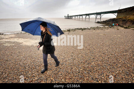 Eine Frau läuft im Regen am Strand neben dem viktorianischen Pier in Clevedon, Somerset. Stockfoto