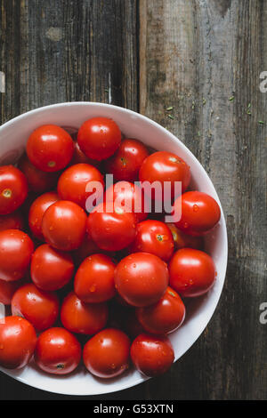 Cherry-Tomaten mit Wassertropfen in Schüssel auf rustikalen hölzernen Hintergrund weiß bedeckt. Ansicht von oben, Tiefenschärfe, getönten Bild Stockfoto