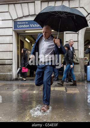 Menschen versuchen, eine große Pfütze außerhalb Victoria Station in London als Starkregen zu vermeiden und grauem Himmel astronomischen Beginn des Sommers getrübt haben. Stockfoto