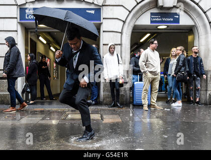 Menschen versuchen, eine große Pfütze außerhalb Victoria Station in London als Starkregen zu vermeiden und grauem Himmel astronomischen Beginn des Sommers getrübt haben. Stockfoto