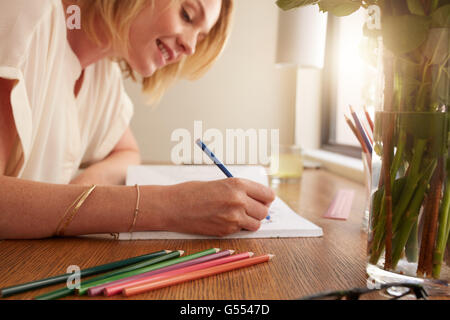 Nahaufnahme des entspannten Frau Färbung Erwachsener Malbuch mit Stiften, sie sitzt auf einem Tisch zu Hause. Stockfoto