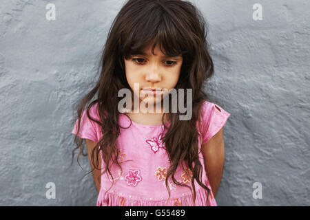 Porträt von kleinen Mädchen stehen auf der Suche verärgert hautnah. Traurige junge Mädchen stehen gegen eine graue Wand. Stockfoto