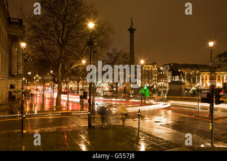 London, England, dem Trafalgar Square in der Nacht bei Regen, Auto helle Streifen und Menschen mit Regenschirmen Stockfoto