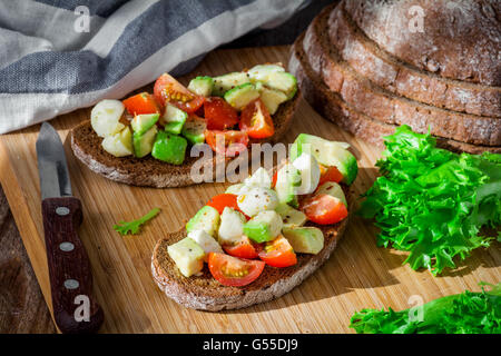 Bruschetta mit Tomaten, Avocado und Weichkäse auf Holzbrett. Gesunde snacks Stockfoto