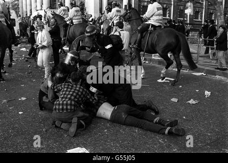 Polizeibeamte betreuen einen verletzten Mann am Trafalgar Square, London, nachdem eine Anti-Umfrage-Steuerdemonstration zu einem Aufruhr verkommen war. Berittene Polizeibeamte können in Richtung Charing Cross Rd. Gesehen werden Stockfoto