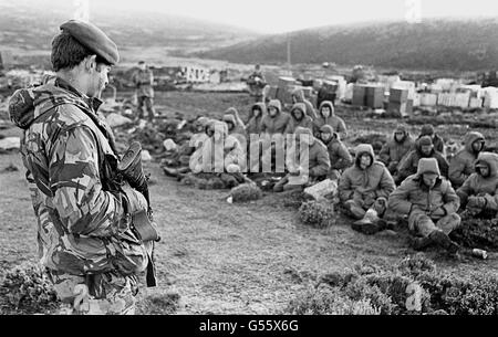 DER FALKLANDKRIEG 1982: Argentinische Soldaten, die bei Goose Green gefangen genommen wurden, werden von einer britischen Royal Marine bewacht, während sie auf den Transit aus dem Gebiet warten. Goose Green wurde von Männern des Fallschirmregiments, Teil der britischen Task Force, gefangen genommen. 825/03/02 Argentinische Soldaten gefangen bei Goose Green wird von einem britischen Royal Marine bewacht, wie sie den Transit aus dem Bereich warten. Der 20. Jahrestag der Invasion der Falklandinseln durch argentinische Truppen wird am 2. April 2002 stattfinden. Stockfoto