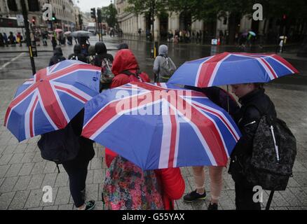 Menschen Sie Unterschlupf unter Sonnenschirmen im Zentrum von London, wie starker Regen und grauem Himmel astronomischen Beginn des Sommers getrübt haben. Stockfoto