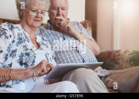 Porträt von ältere Frau sitzt mit ihrem Mann und mit digital-Tablette. Ehepaar im Ruhestand auf Sofa zu Hause mit einem Hauch Stockfoto