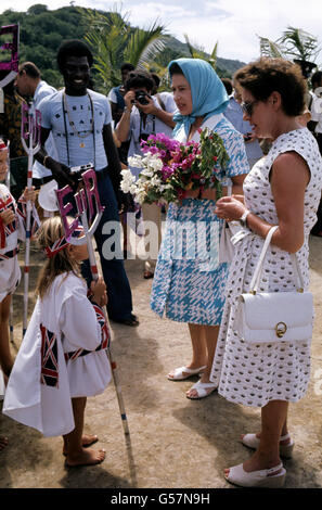 Die Königin, zweite links, erhält von einem jungen Inselbewohner in schickem Kleid auf der Insel Mustique ein schickes Kleid. Mit ihr ist ihre Schwester, Prinzessin Margaret, die eine Villa auf der Insel hat. Stockfoto