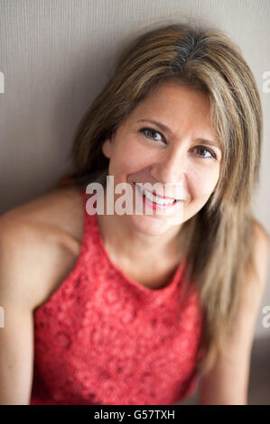 Schließen Sie sich ziemlich 50 Jahre alte Frau lehnt sich gegen die Wand und man die Kamera mit glücklichen Gesichtsausdruck. Stockfoto