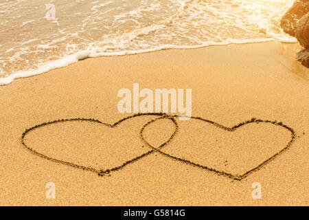 Ein paar Herzen am Sandstrand mit der weichen Welle gezogen. Stockfoto