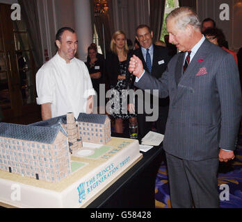 Der Prinz von Wales hält ein Messer in der Hand, als er Chef Gary Hollihead (links) fragt, wie er den Kuchen - von Stanley Mills in Perth - schneiden sollte, während er an einem Empfang anlässlich des 15-jährigen Jubiläums des Prince's Regeneration Trust im Corinthia Hotel, London, teilnimmt. Stockfoto