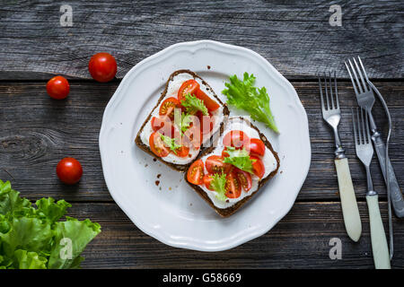 Teller mit gesunden Toast mit Cherry-Tomaten und Ricotta-Käse auf Vollkorn Roggenbrot, rustikalen hölzernen Hintergrund, Tisch-Draufsicht Stockfoto