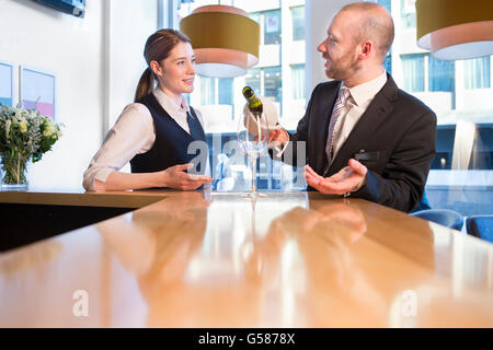 Kellnerin an der Bar stehen anhören des Managers, da er ein Glas Champagner gießt Stockfoto