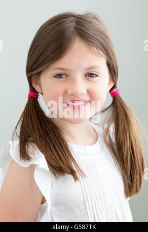 Porträt eines jungen Mädchens. Sie hat ihr Haar in Zöpfen und lächelt in die Kamera gegen eine einfache blackground Stockfoto