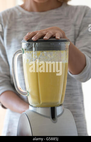 Blick auf ein Womans hautnah die Hände auf einen Mixer, mischen Sie einen Frucht-Smoothie. Stockfoto