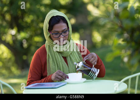 Frau genießen einen Kaffee in ihrem Garten an einem sonnigen Morgen. Stockfoto