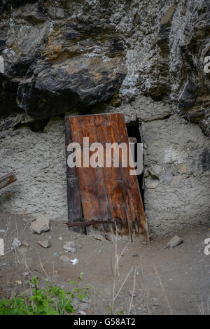 alte Holztür in Felswand neben einer Straße in Schweizer Alpen Stockfoto