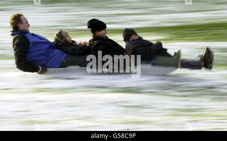 Kinder und Erwachsene nutzen das winterliche Wetter, während sie im Greenwich Park, South London, im Schnee reiten. Stockfoto