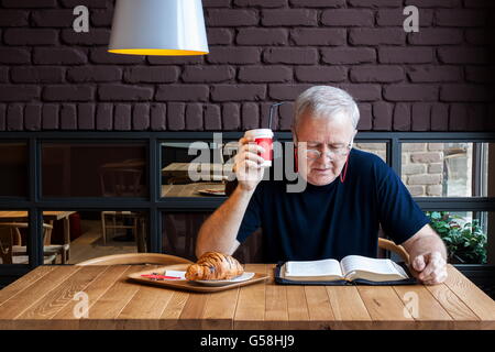 Man sitzt an einem Tisch mit einem Kaffee und ein Croissant in einer Snack-Bar und die Bibel zu lesen. Arbeiten gewidmet geistige Pause Stockfoto