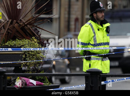 Ein Polizist steht in der Nähe von Blumen in einer Absperrung nahe der Szene eines vermuteten Gases in der Buckley Street im Shaw-Gebiet von Oldham, Greater Manchester, bei dem der zweijährige Jamie Heaton getötet wurde und Anthony Partington, 27, Wurde mit lebensbedrohlichen Verbrennungen verlassen, nachdem drei Reihenhäuser zu Schutt reduziert wurden. Stockfoto