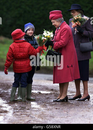 Königin Elizabeth II. Nimmt Blumen von Joseph Burton, neun, und seiner siebenjährigen Schwester vor der St. Peter, St. Paul Church in West Newton, Norfolk, entgegen. * Ein moderner Walter Raleigh war nirgends zu sehen, als die Königin beim Verlassen der Kirche eine Reihe kniffliger Pfützen aushandelte. Die Jugendlichen, beide mit grünen Wellingtons, brachen das königliche Protokoll, indem sie unter eine Barriere gingen und in eine Pfütze gingen, um der Königin Blumensträuße zu geben. Stockfoto