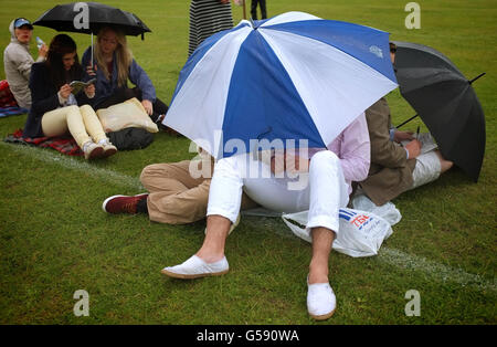 Tennisspieler schützen sich am siebten Tag der Wimbledon Championships 2012 im All England Lawn Tennis Club, Wimbledon, unter Regenschirmen vor Regen. Stockfoto