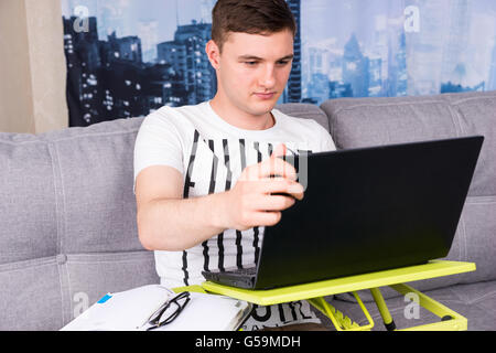 Ernsthafte schönen jungen Mann arbeitet an einem Laptop sein Geschäft von zu Hause aus tun, da er Informationen auf dem Bildschirm liest Stockfoto