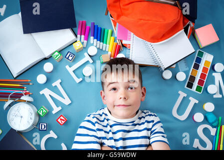 Kind auf blaue Decke liegend mit Schule Zubehör Stockfoto