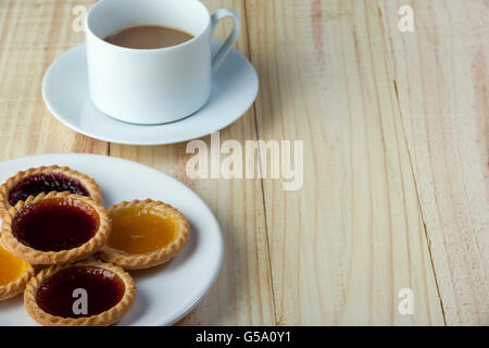Teller mit sortierten frische Marmelade Kuchen auf einem Holztisch mit einer Tasse Milchkaffee Stockfoto