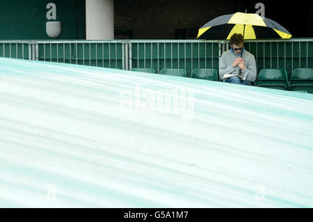 Ein Tennisfan schützt vor Regen, da das Spiel am achten Tag der Wimbledon Championships 2012 im All England Lawn Tennis Club in Wimbledon gestoppt wird. Stockfoto