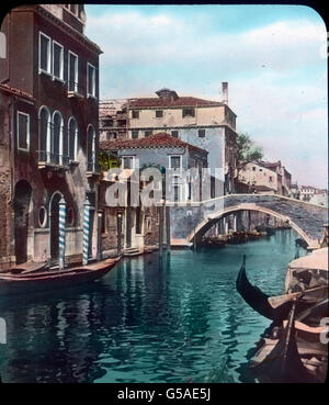 Die ganze Schönheit eines kleinen Kanals zeigt uns dieses Bild. Farbprächtig umrahmt von hohen Häusern und prunkenden Palästen, die er in seinem klaren Wasser widergespiegelt. Travel, Italy, Venice, Venetia, Veneto, history, Historical, Archive, Carl Simon, 1910s, 20th century, Canal, Waterway, Street, House, Building, architecture, Gondel, traffic, Canal, Giovanni e Paolo, Hand colored glass slide Stockfoto