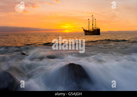 Meer Sonnenuntergang Schiff Fantasy ist ein hell erleuchteter golden Seelandschaft mit einem Piratenschiff verankert auf hoher See mit dem Vollmond steigt in die Stockfoto