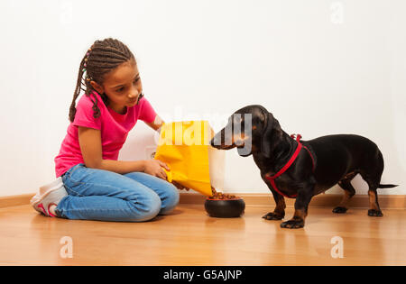 Schwarze Mädchen, die ihr Haustier Hund mit der Nahrung zu füttern Stockfoto