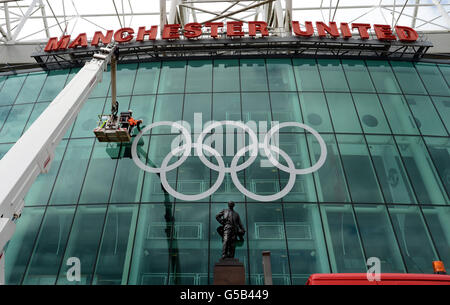 Riesige olympische Ringe sind hinter der Statue von Sir Matt Busby auf der Vorderseite des Old Trafford Football Ground, Heimat von Manchester United, in Manchester platziert. Stockfoto