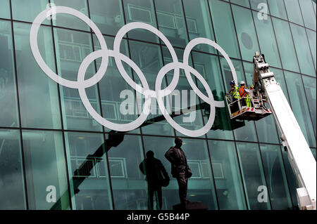 Riesige olympische Ringe sind hinter der Statue von Sir Matt Busby auf der Vorderseite des Old Trafford Football Ground, Heimat von Manchester United, in Manchester platziert. Stockfoto