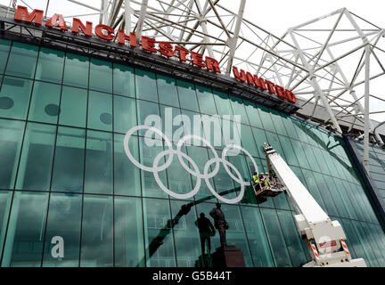 Riesige olympische Ringe sind hinter der Statue von Sir Matt Busby auf der Vorderseite des Old Trafford Football Ground, Heimat von Manchester United, in Manchester platziert. Stockfoto