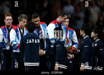 Die Briten (von links nach rechts) Daniel Purvis, Max Whitlock, Louis Smith, Kristian Thomas und Sam Oldham schütteln sich die Hände mit der silbernen Medaille siegreichen japanischen Mannschaft auf dem Podium, nachdem sie die Bronzemedaillen während des Finales des Artistic Turnen Teams in der North Greenwich Arena, London, gewonnen hatten. Am dritten Tag der Olympischen Spiele 2012 in London. Stockfoto