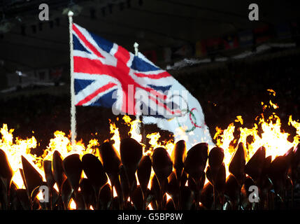 Olympische Spiele In London - Tag 10. Die Union Jack Flag und die Olympic Rings Flag fliegen im Hintergrund der Olympic Flame im Olympiastadion in London. Stockfoto